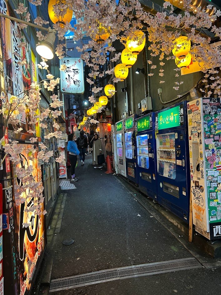 The vibrant atmosphere of Omoide Yokocho at night, illuminated by colorful lanterns and restaurant signs.